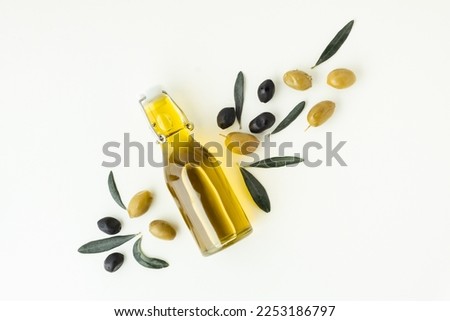 Green and black olives in white bowls next to a bottle with olive oil and leaves on a white background. 
Bottle of cold pressed oil. Traditional Greek and Italian food. Flat lay.