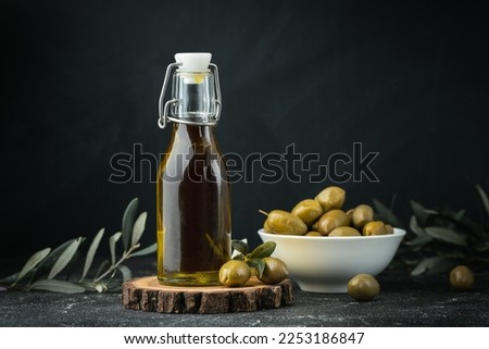 Green olives in a white bowl next to a bottle with olive oil and leaves on a black background. Bottle of cold pressed oil. Traditional Greek and Italian food.