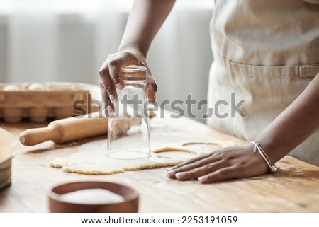 Close up of black woman baking homemade pastry and cutting cookie shapes on wooden kitchen counter, copy space
