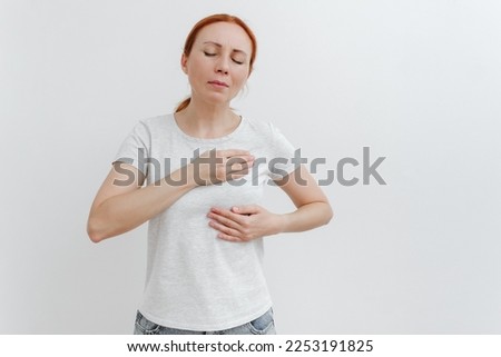 Young caucasian woman feeling breast pain, touching her chest. Brest cancer. White background, studio shoot.