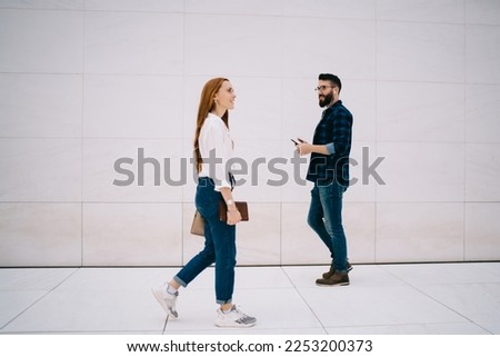 Full body side view of smart casual man and woman passing each other while walking along blank tiled wall on street sidewalk Royalty-Free Stock Photo #2253200373