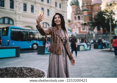 Cheerful female travel blogger shooting influence vlog with web sightseeing during solo vacations in Moscow, smiling Asian tourist in earbuds making international video call for communicate in roaming