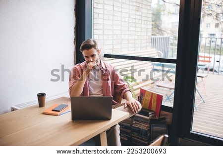 Caucasian software developer in bluetooth earphones watching webinar video on modern netbook device using coworking WIFI internet connection during distance job, skilled programmer analyzing data code