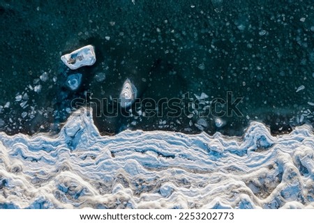 Top view of the freezing sea. Winter aerial photograph of the icy coast and ice floes in sea water. Nature of the Extreme North. Cold frosty winter weather. Harsh arctic climate. Natural background. Royalty-Free Stock Photo #2253202773