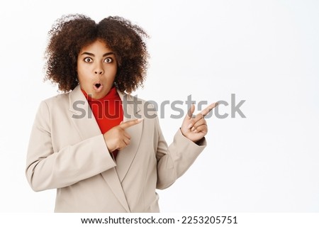 Surprised african american businesswoman, looks amazed, say wow and point right at direction, shows banner or company logo, advertising, standing over white background.