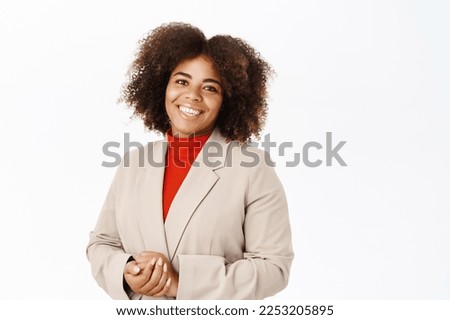 Smiling african american businesswoman in suit, looking friendly at client, ready to help and answer questions, standing over white background.