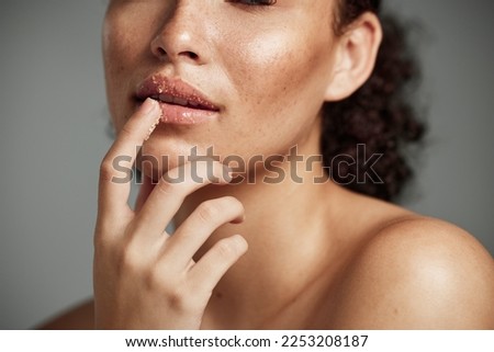 Woman, hand and lips in sugar scrub for skincare, makeup or cosmetics against a grey studio background. Happy female applying treatment for facial cosmetic, lip dermatology or mouth exfoliation Royalty-Free Stock Photo #2253208187
