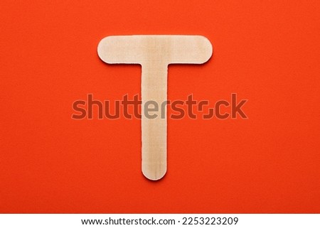 White wooden capital letter T on orange foamy background