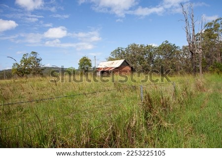 A photo of a deserted shack or cabin with broken walls and a rusty roof in an overgrown field.  Royalty-Free Stock Photo #2253225105