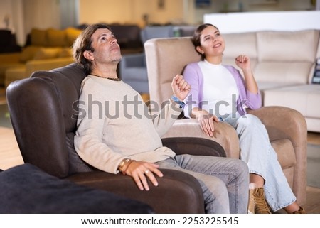 Trying new armchairs. Man in beige sweater and young woman sitting in comfortable armchairs