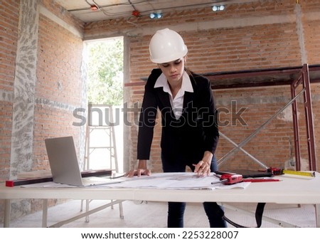 Young caucasian architect woman looking laptop and working drawing blueprint for planning building house on desk, engineer thinking and sketching blueprint for construction, industrial concept.