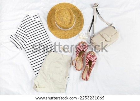 White t shirt, shorts, straw hat, sandals, bag on white background. Top view of woman's spring casual outfit. Simple basic summer women clothes. Flat lay. Royalty-Free Stock Photo #2253231065