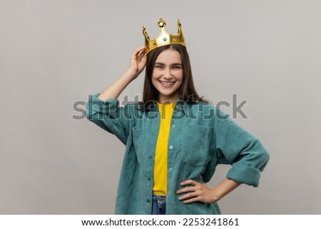 Woman in crown on head looking at with confident expression, self-motivation and dreams to be best. keeping hand on hip, wearing casual style jacket. Indoor studio shot isolated on gray background. Royalty-Free Stock Photo #2253241861