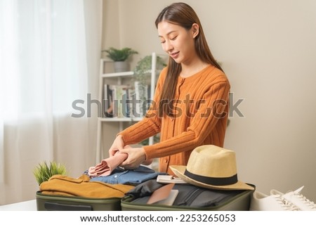 Vacation, holiday travel, traveler asian young woman, girl hand folding clothes packing and preparing stuff into luggage or baggage bag case for journey trip, preparation for journey voyage at home. Royalty-Free Stock Photo #2253265053