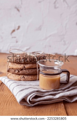 Cup of coffee with milk and cookies with chocolate pieces on the brown wooden table