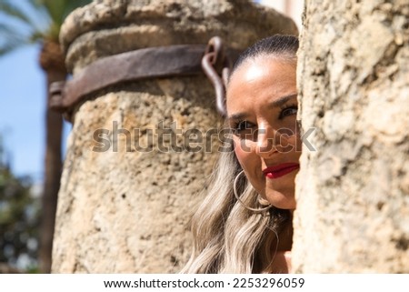 Young and beautiful blonde Spanish woman is between two columns of the cathedral of Seville. The woman is dressed in modern clothes and is happy. The woman is sightseeing and visiting spain.