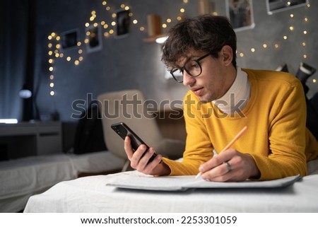 Arabic young guy college student holding smartphone studying on cell, distance learning using apps for education, e learning on mobile phone in university campus at night. Copy space Royalty-Free Stock Photo #2253301059