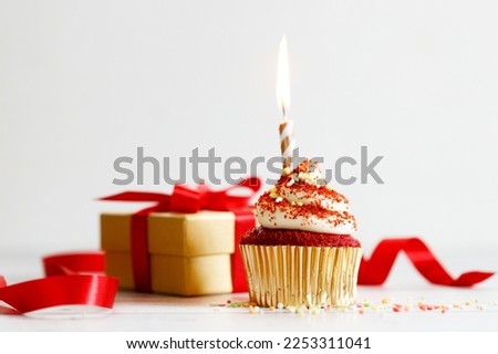 red velvet cupcake top with white cream cheese frosting with candle on wooden table background.