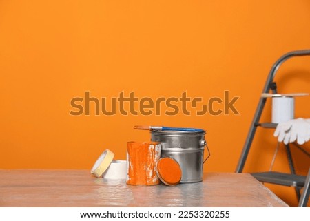 Can with paint, brush and renovation equipment on table against orange background. Space for text