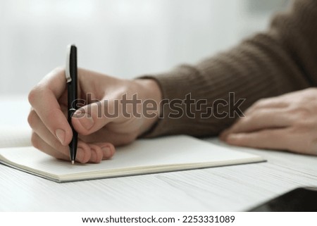 Man writing in notebook at white wooden table, closeup