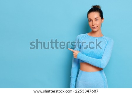 Photo of pretty lady in sportswear, index fingers direct to empty space showing banner, isolated over blue color background