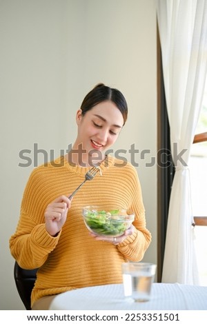 Portrait, Pretty and charming millennial Asian woman enjoys eating healthy salad vegetables mix at dining table in beautiful minimal dining room. Royalty-Free Stock Photo #2253351501