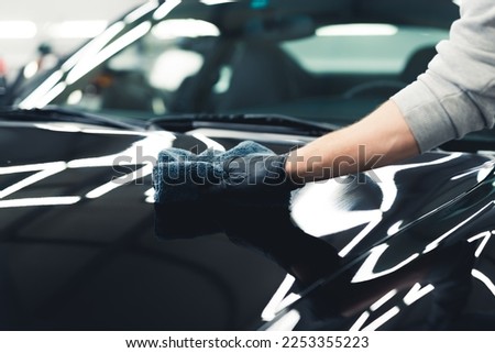 Unrecognisable man wearing black gloves applying ceramic coating to the front of black car. Professional car detailing process. Horizontal indoor shot. High quality photo