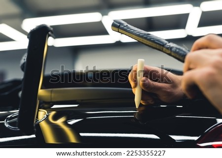 Close-up shot of dents being removed from body of car with professional equipment inside garage. Car repair and detailing. Horizontal indoor shot. High quality photo