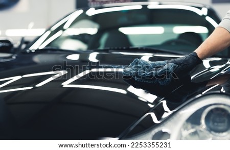 Close-up shot of man wearing black glove applying ceramic coating to hood of black car. Professional car detailing. Horizontal indoor shot. High quality photo