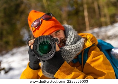 Portrait of a photographer taking winter photos in the mountains with snow doing a trekking with a backpack