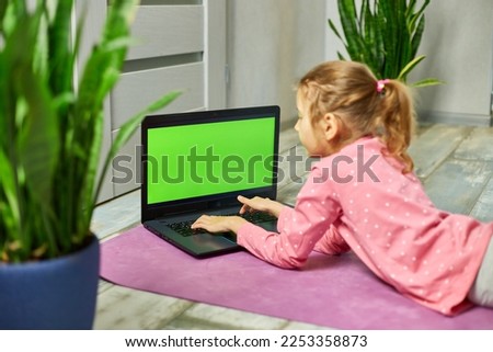 Little girl watching online video on laptop green screen doing stretching, fitness exercises at home. Child distant training with personal trainer, online education concept, Playing sports, Healthy 