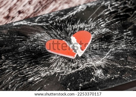 A torn red cut out paper heart on a shattered black glass smartphone screen