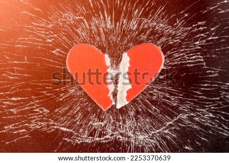 A torn red paper heart on a broken cracked black smartphone glass 