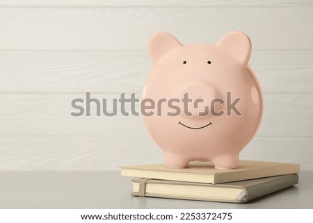 Ceramic piggy bank and notebooks on light grey table. Space for text