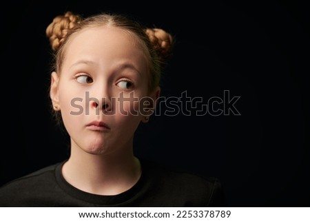 Portrait of a beautiful funny girl in a black t-shirt on a black studio background with copy space. Children, emotions. Psychological picture.