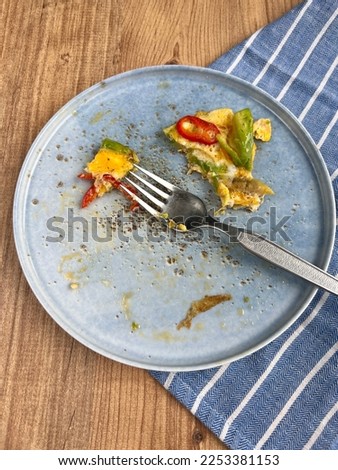 leftovers of breakfast omlette on plate on a wooden table. blue plate on table with food leftovers. breakfast or health food consumption concept photo on wooden background Royalty-Free Stock Photo #2253381153