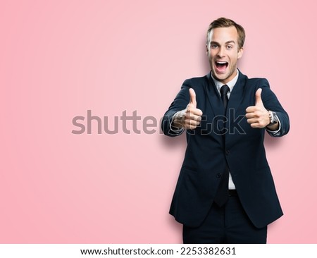 Happy excited businessman showing two thumbs up like hand gesture, in black confident suit, over rose pink color background. Very cheerful man. Copy space for ad, slogan or text.