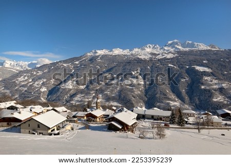  alpine village with snowy roofs in tarentaise valley view on snowcapped mountains under blue sky  Royalty-Free Stock Photo #2253395239
