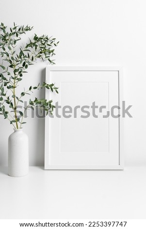 White portrait frame mockup in scandinavian room with green eucalyptus twig in vase, blank mockup with copy space