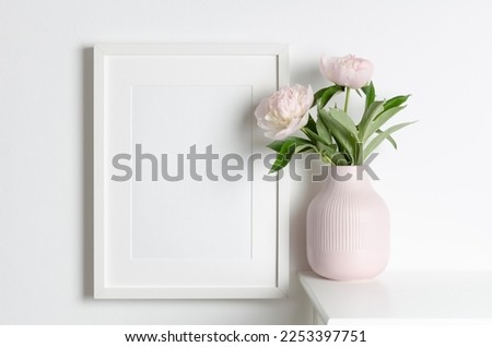 Frame mockup on white wall with pink peony flowers in vase, blank mockup for artwork presentation