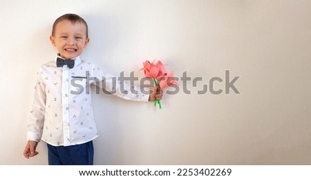 A little boy is holding a bouquet of pink tulips made of colored paper, origami on a white background. The concept of a gift for mom on March 8, mother's day or birthday. Banner with space for text