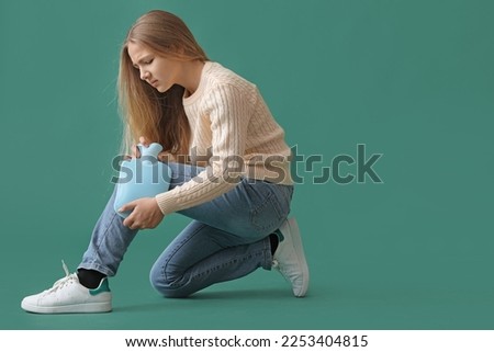 Ill girl warming her knee with hot water bottle on green background