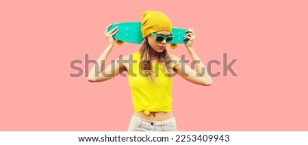 Summer portrait of stylish cool young woman with skateboard wearing colorful clothes on pink background