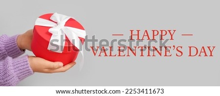 Greeting card for Valentine's Day with hands holding gift on light background
