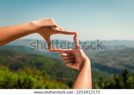 hand framing view distant over sunset on mountain Royalty-Free Stock Photo #2253413173