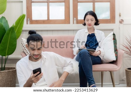 Young couple working together at home. woman sit on sofa with tablet and man watching on phone. Creative office colleagues discuss the new idea and storyboard in living room.