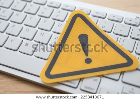 Yellow alert sign on white keyboard on wooden table background. Online internet, network security or computer problem concept. Attacked from hacker via virus computer, malware, spam, trojan or spyware