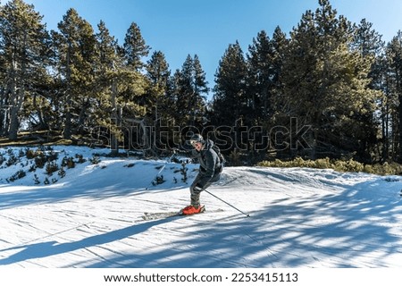 An adult boy, dressed in ski clothes and equipment, is skiing and skidding on a flat, straight track through a beautiful mountain forest during the cold winter season.