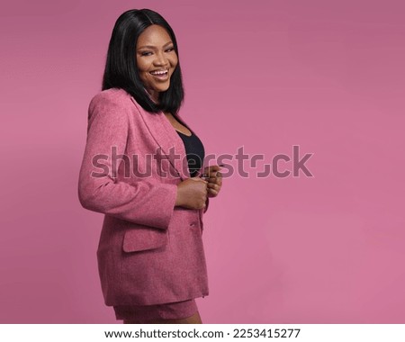 Happy confident professional posing Over a Pink Background. Young African American business woman  adjusting formal jacket, looking at camera, smiling. Successful businesswoman concept Royalty-Free Stock Photo #2253415277
