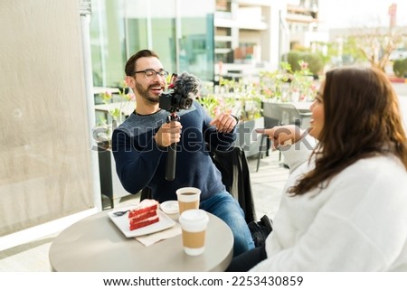 Excited caucasian man filming an influencer big woman making social media content at a coffee shop or restaurant